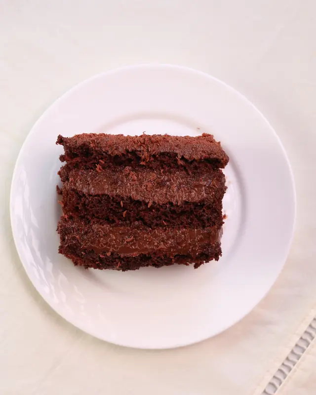 Fatia de bolo de chocolate em três camadas vista de cima, num prato branco