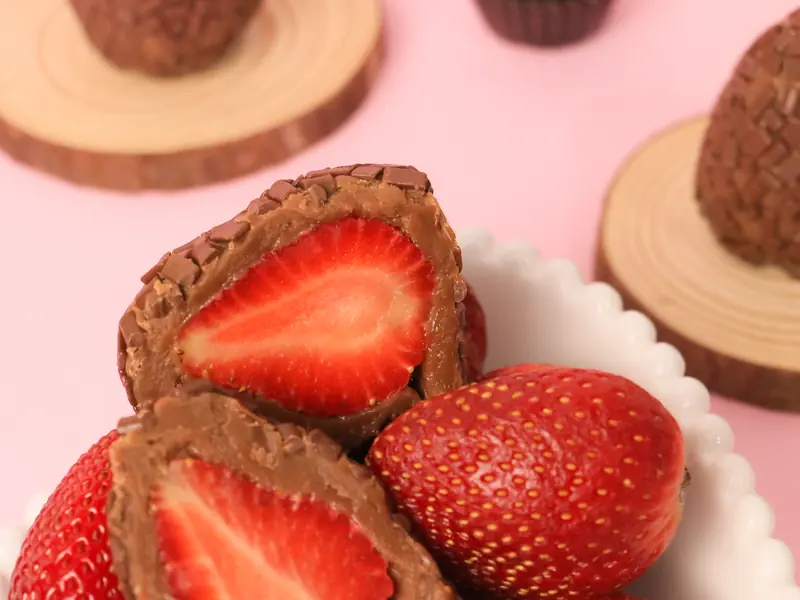 Vários morangos com brigadeiro, cortados ao meio, numa travessa branca com morangos inteiros