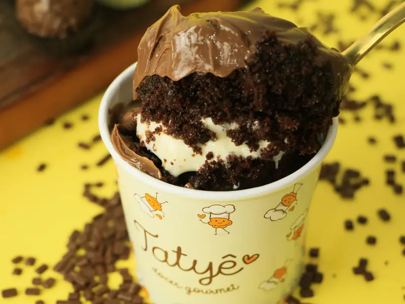 Pote da Tatyê com sobremesa de chocolate e creme branco, com uma colher tirando uma porção, sobre fundo amarelo